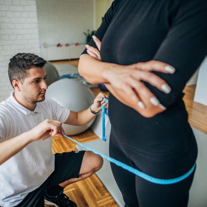 a man measuring a lady's thighs in a gym