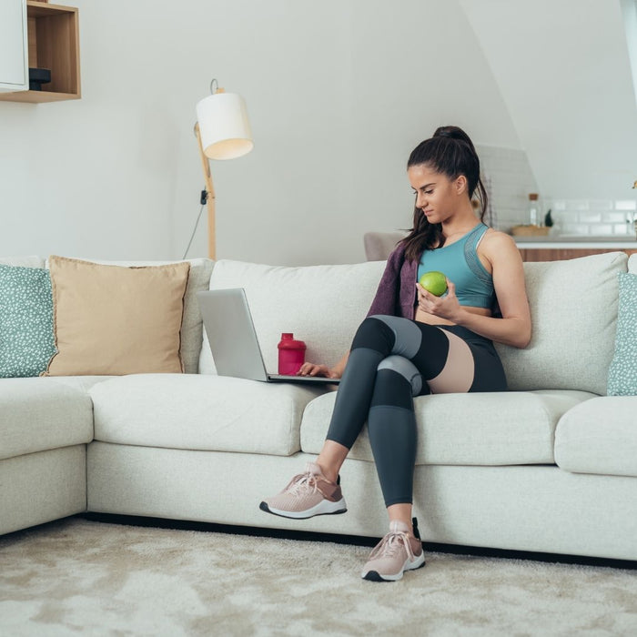 a woman eating a healthy apple looking at laptop in fitness gear