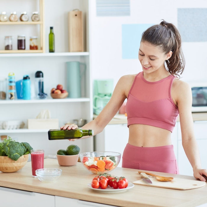 a woman pouring salad dressing over veg bowl before working out