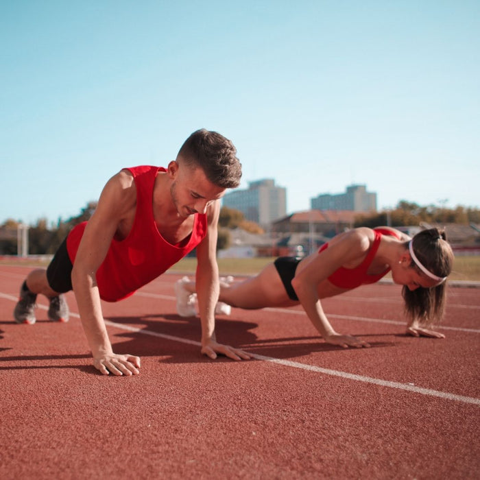 A man and a woman are doing pushups on a track